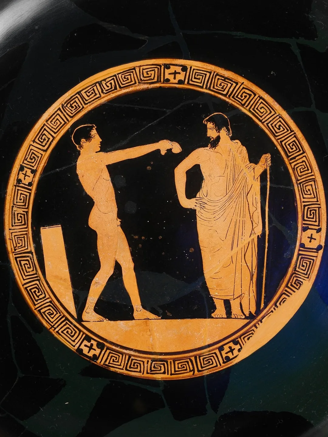 Greek drinking cup showing a young athlete stretching out his arm towards an older man holding a staff